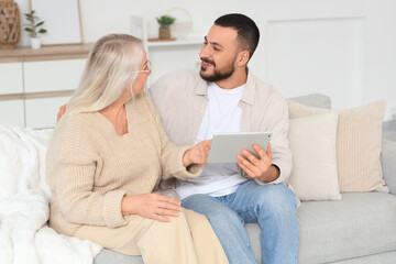 Young man with tablet computer hugging his mother on sofa at home