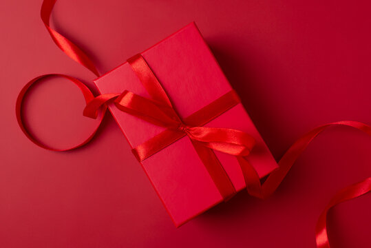 Xmas gift box and decoration celebration in Christmas theme. Red present box on red background. Valentines day gift box with red ribbon. Monochrome color scheme, top view