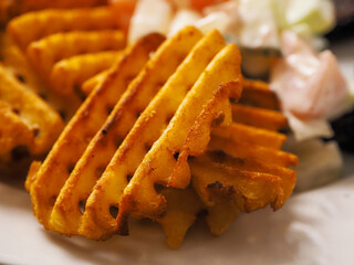 Cooked potato chips fries in a lattice shape on a white plate. Selective focus. Marketing move to sell popular product with increased price for higher profit by just changing the look.