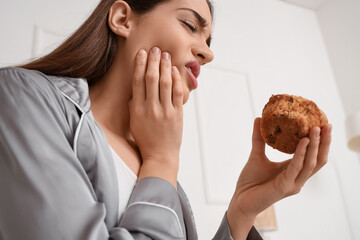 Young woman in pajamas with muffin suffering from toothache at home, closeup