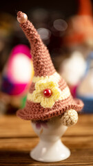 A whimsical crochet gnome cap with yellow flower accent, perched on a white ceramic holder, perfectly blending playful craftsmanship with a charming artistic touch.