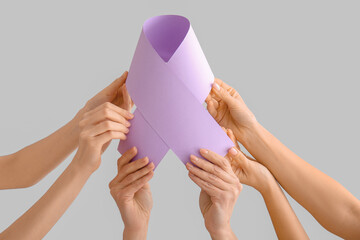 Hands holding paper awareness ribbon on grey background