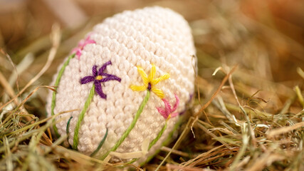 A handmade crocheted egg with vibrant floral embroidery rests gently on a lush bed of hay, evoking themes of nature, craftsmanship, and creativity.
