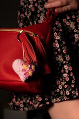 A stylish red handbag adorned with a floral crocheted heart accessory showcases a chic combination of fashion and handmade elegance for modern style enthusiasts.