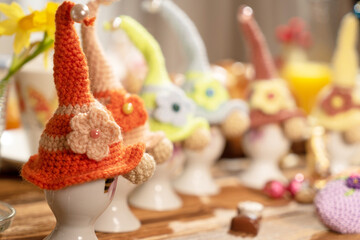 A whimsical display of colorful, handcrafted knit hats perched on egg holders, set against a backdrop of vibrant, festive decorations perfect for Easter celebrations.