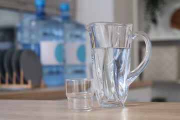 Jug of clean water with glass on table in kitchen, closeup