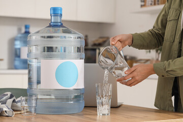 Woman pouring clean water into glass on table in kitchen
