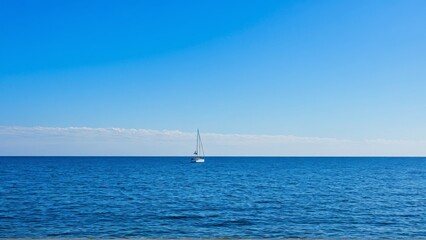 Fototapeta premium Serene sailboat on tranquil blue sea under clear sky