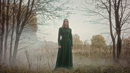 Model posing in misty forest wearing long green