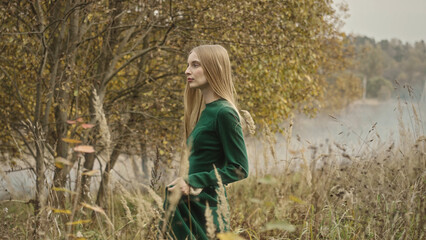 Fashion model posing in autumn landscape near lake