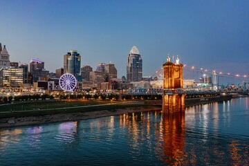 Evening cityscape of downtown Cincinnati, featuring the illuminated Roebling Suspension Bridge...