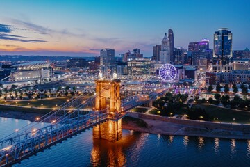 Fototapeta premium Evening cityscape view of the Cincinnati skyline, featuring the iconic Roebling Suspension Bridge at twilight. Downtown, Cincinnati, Ohio, United States
