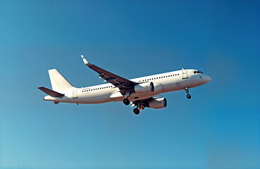 Obraz premium White a320 neo jet aircraft glides through clear blue sky. Modern passenger plane in process of landing. Aircraft nearing ground. Safe, smooth landing evident. Bright daytime shot shows high quality