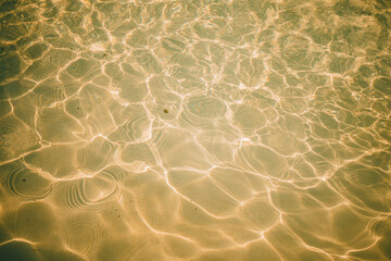Sunlight reflecting on clear water with shimmering ripples, creating intricate patterns and golden hues. Ideal for backgrounds, textures, or aquatic themes.
