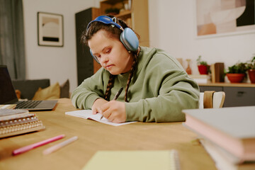 Caucasian girl with Down syndrome listening to music in headphones while studying in living room at...