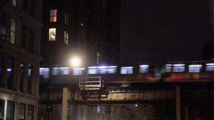 CHICAGO - 12.5.2024 - An elevated train enters a passage between apartment buildings in Chicago at night.
