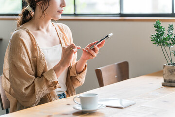 カフェでコーヒーを飲みながらスマホを見る若いアジア人女性（待ち合わせ）
