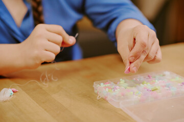 Closeup of hands of unrecognizable woman beading accessory, sitting at wooden table at home