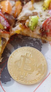 Vertical video. Golden Bitcoin Coin Placed on a Tray Next to a Partially Eaten Pizza with Vegetables and Pepperoni from Close-Up Perspective. Concept of Digital Currency and Food Purchase.