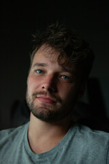 Fototapeta premium A close-up indoor portrait of a man with a calm and relaxed expression, soft lighting accentuating his features. The blurred background with colorful artwork adds warmth and depth to the image