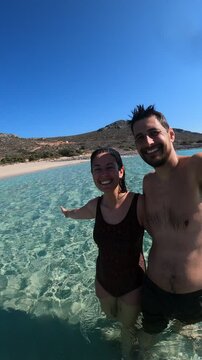Selfie view of couple inside turquoise water sea beach in Greece panning the camera in Simos beach in Elafonisos island, in Greece