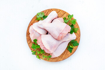 Raw chicken legs on round wooden board with pepper, salt and parsley. White background, top view