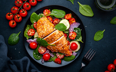 Healthy vegetable salad with spinach, grilled chicken, tomatoes, cucumber and red onion. Black table, top view