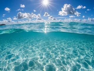 Sunlit ocean surface and underwater view showing clear turquoise water, bright sun, and fluffy clouds.