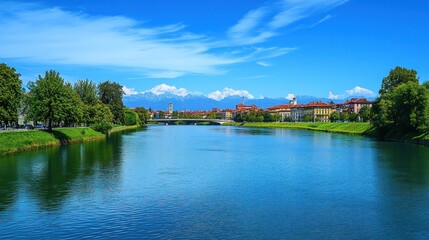 River view of a city with mountains in the background under a blue sky.