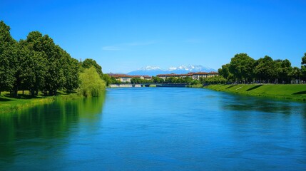 Fototapeta premium Serene river scene with cityscape and mountains under a clear blue sky.