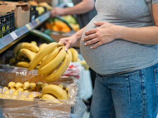 Pregnant woman buys bananas in the store. 