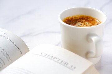 テーブルの上の開いたペーパーバック（洋書）と、コーヒーの入ったコーヒーカップで、コーヒーを飲みながらゆっくりと読書を楽しんでいるイメージ

