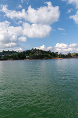 Serene lake view under a bright, puffy sky. Lush greenery and a tranquil atmosphere.