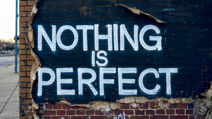 White graffiti on a black brick wall reads Nothing is Perfect..