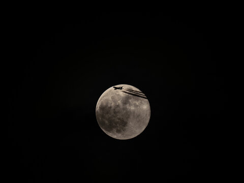 The moon in the night sky with a silhouette of an airplane. The moon in the dark sky with a plane flying over it.
