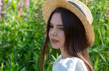 Portrait of a brunette girl in a straw hat outdoors in summer