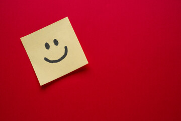 Smiley face emoji drawing on sticky note paper on red background