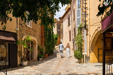 Obraz premium A nicely dressed young couple walk through the narrow streets of the medieval hill town of Grimaud, France, in the hills above St Tropez on the French Riviera.