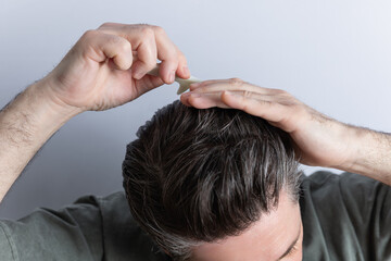 Close-up of unrecognizable man combing his toupee with his hands and a comb. Isolated on gray background. Hair styling and hair care concept