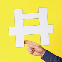 Obraz premium A hand of a Caucasian male holding a large white hashtag symbol against a vibrant yellow background.