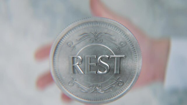 A hand flips a coin marked Work and Rest, spinning toward the camera in slow motion