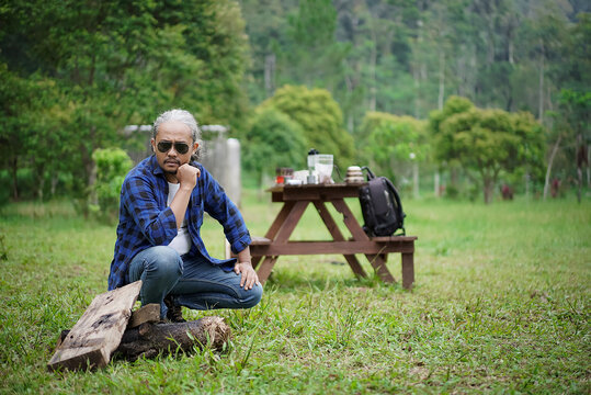 Indonesian male traveler with curly hair making a campfire while traveling in the forest, travel concept.