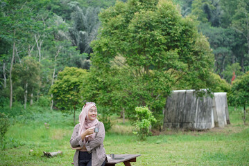Young Indonesian woman wearing hijab enjoying the calming natural atmosphere while enjoying a cup of black coffee, away from the hustle and bustle of the city, travel concept.