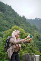 young indonesian female traveler wearing hijab taking photos while traveling in nature, travel concept.