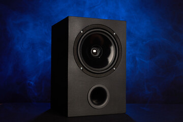 Black full-range speaker with bass reflex on blue background with smoke.