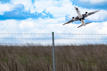 Passenger plane maneuvering in cloudy sky. Aircraft behind barbed wire. Country border. Illegal...