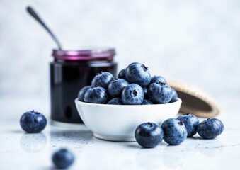 A bowl of blueberries sits on a table next to a jar of blueberry jam