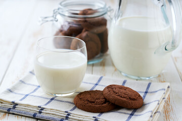 Glass and a jug of fresh milk with delicious chocolate brownie cookies on a white table, selective focus.