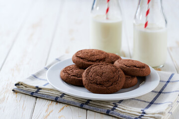 Tasty chocolate cookies and bottles of fresh milk on a light kitchen table, healthy breakfast.