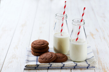 Bottles with fresh milk and chocolate brownie cookies on a on a white table, selective focus.